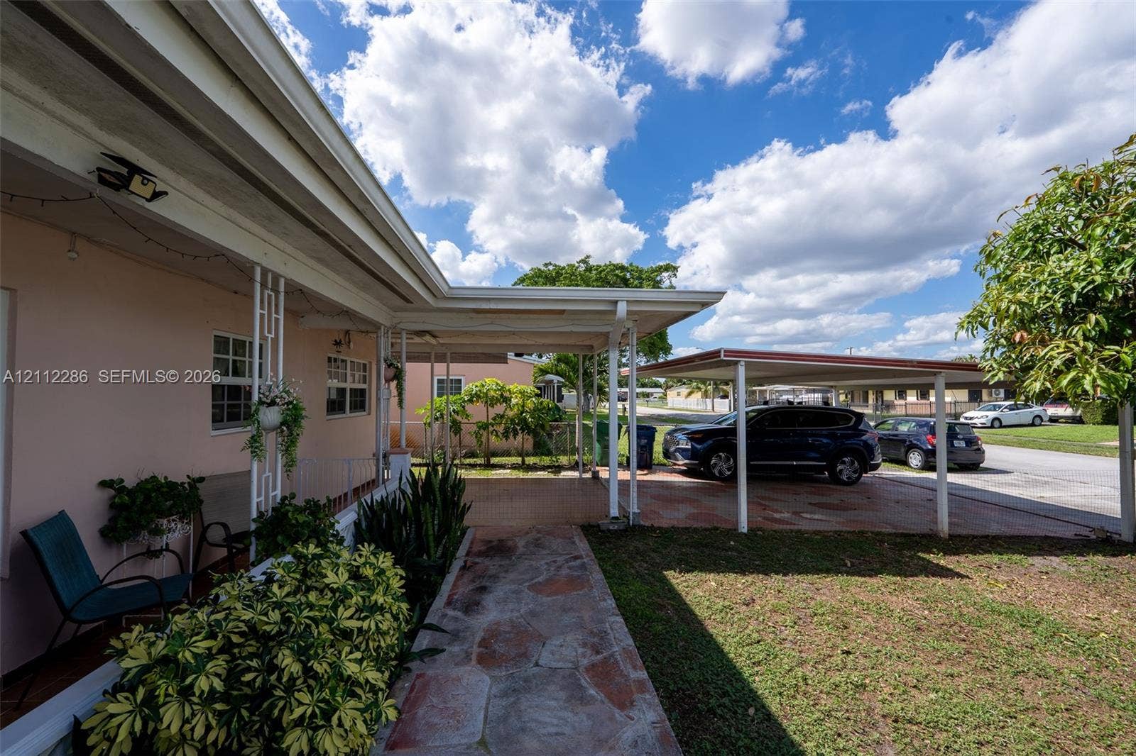 Covered entryway featuring decorative structural columns, stone-paver walkway, and attached carport
