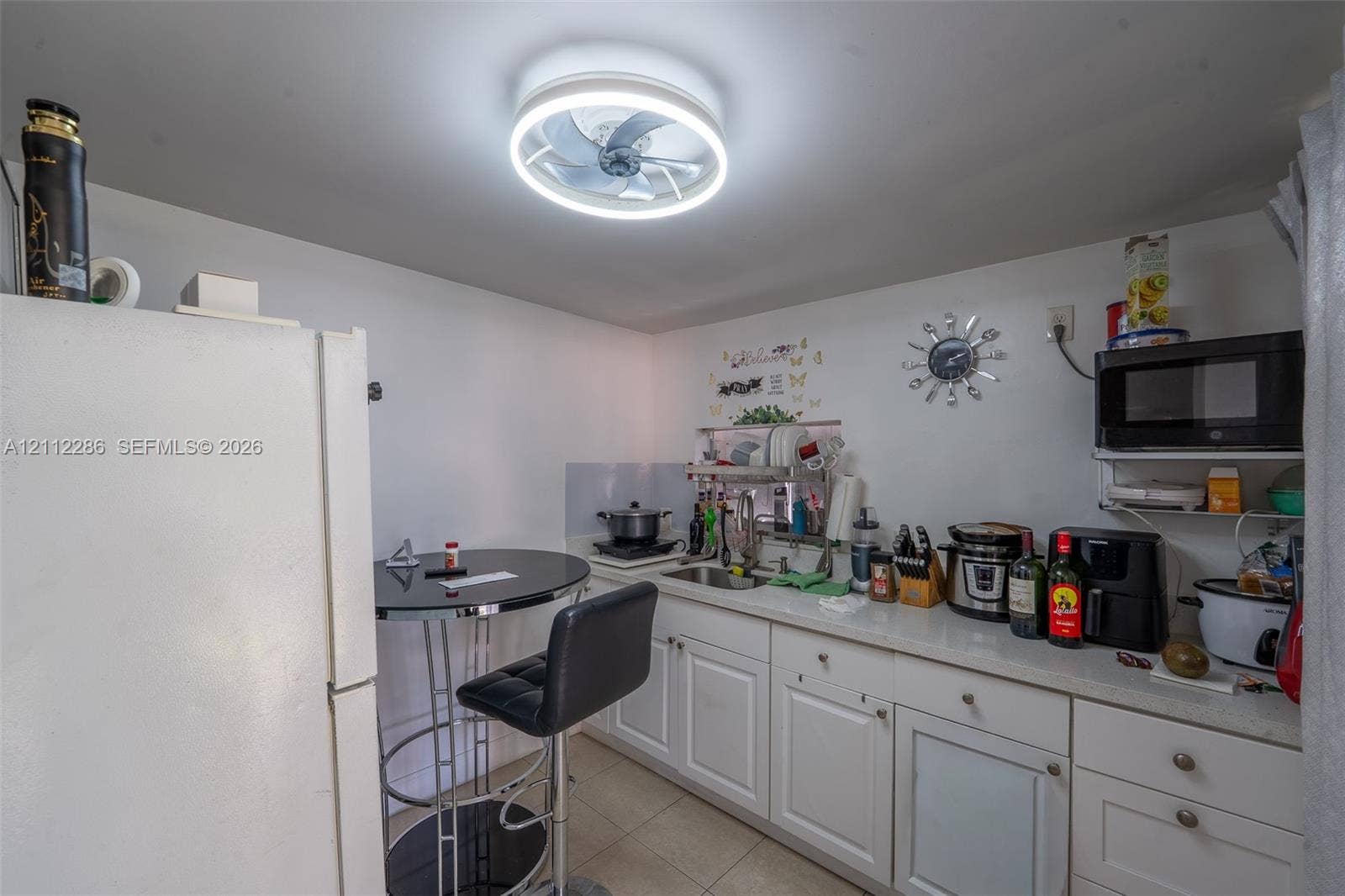 White cabinetry, integrated stainless steel sink, solid-surface countertop, and circular LED ceiling fixture