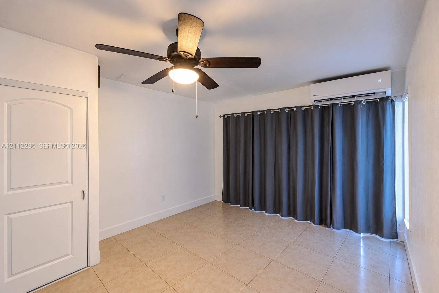Interior space featuring neutral tile flooring, a wall-mounted ductless mini-split air conditioning unit, and a ceiling fan with integrated lighting