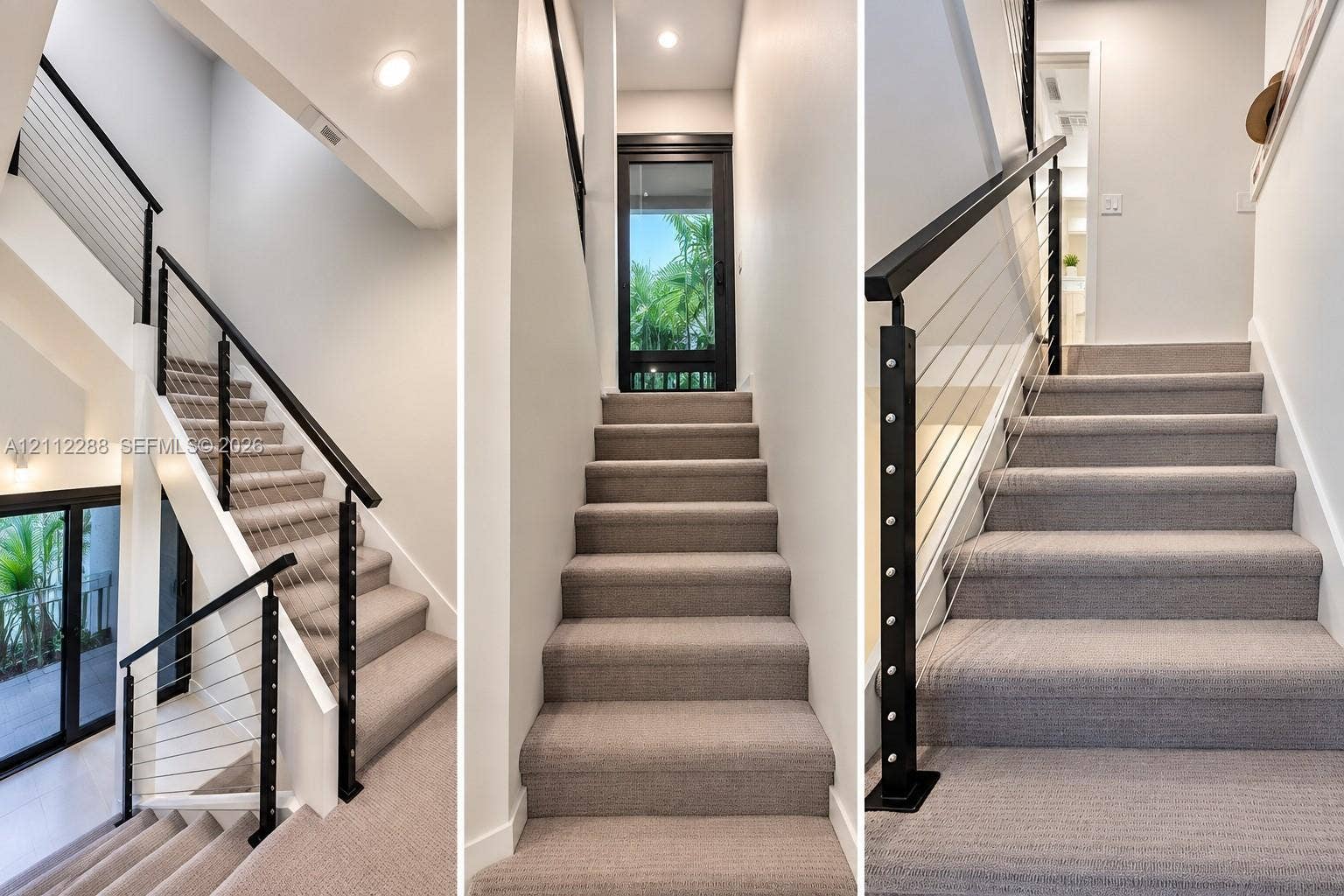 Staircase featuring neutral carpeted treads, a black metal handrail, horizontal cable railing system, and recessed ceiling lighting