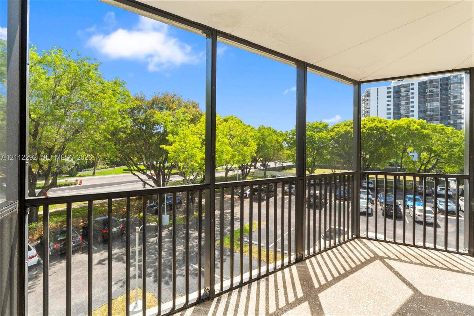Screened balcony featuring a solid surface floor, black metal railing, and overhead lighting