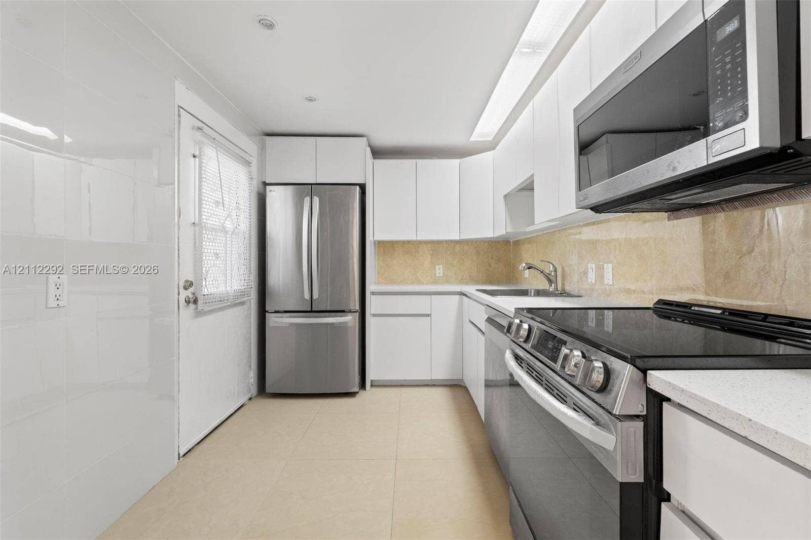 Kitchen featuring white cabinetry, light-toned stone tile backsplash, stainless steel appliances, and tile flooring