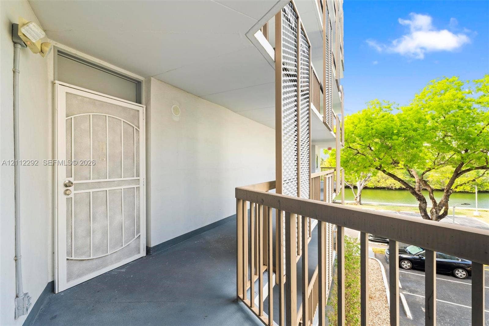 Covered exterior walkway featuring a security screen door, vertical metal railing, and privacy screening