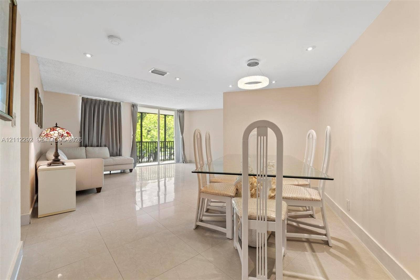 Open-concept interior featuring light-toned tile flooring, recessed ceiling lighting, a modern circular pendant light, and floor-to-ceiling glass sliding doors providing external access
