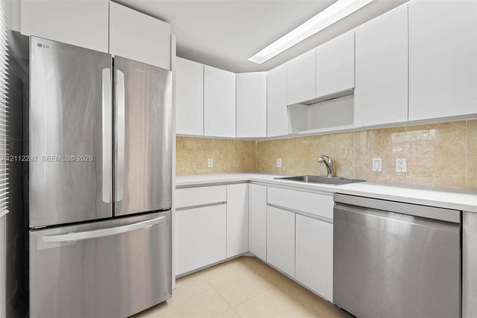 Kitchen featuring flat-panel white cabinetry, stainless steel appliances, neutral stone-finish backsplash, and an undermount sink with a gooseneck faucet
