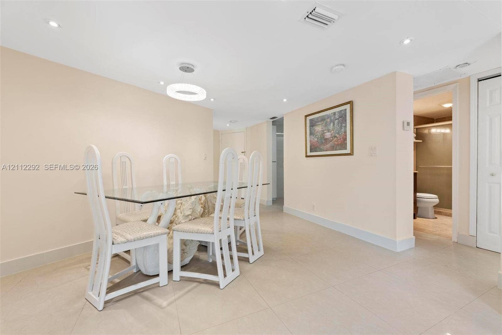 Open-concept area featuring light-toned tile flooring, recessed ceiling lighting, a modern circular LED pendant fixture, and a white paneled door