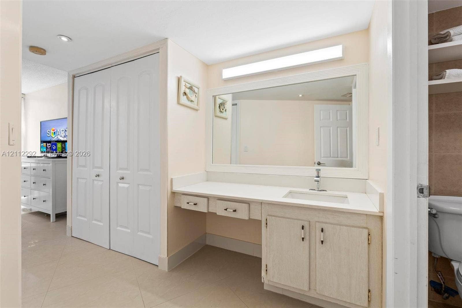 Vanity with integrated sink and countertop, full-width mirror, light-toned cabinetry, and dual-door closet