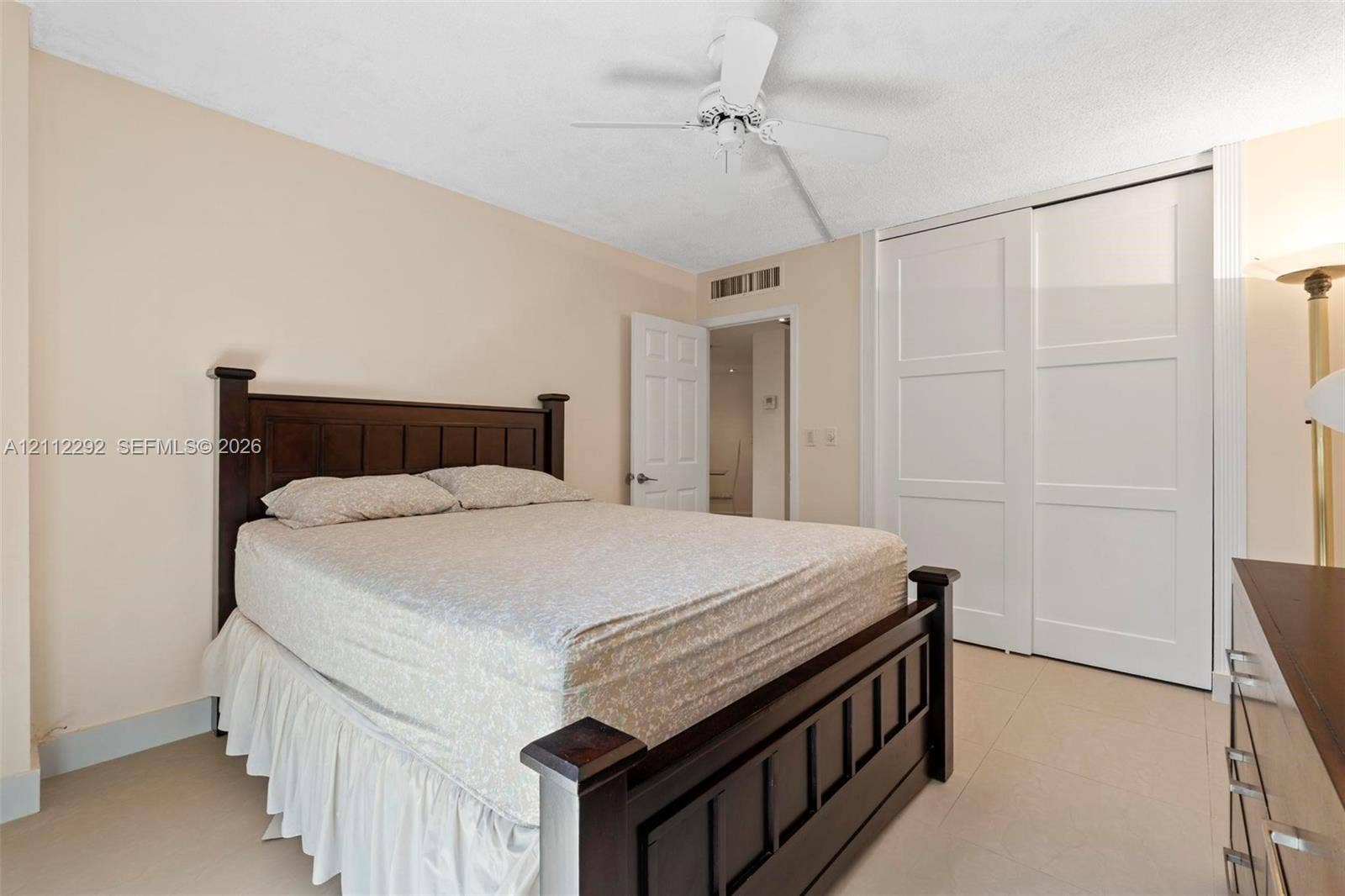 Neutral-toned room featuring tile flooring, a white ceiling fan, and sliding panel closet doors