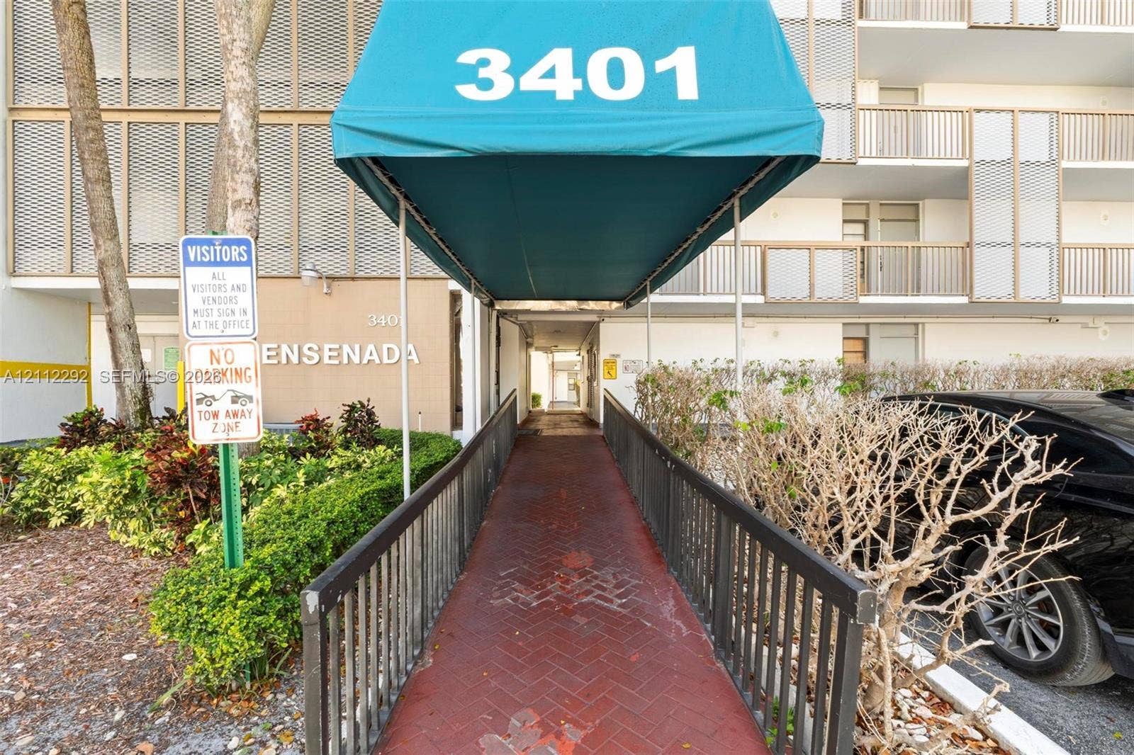 Covered entrance featuring a teal canopy, brick-paver walkway, and metal railing