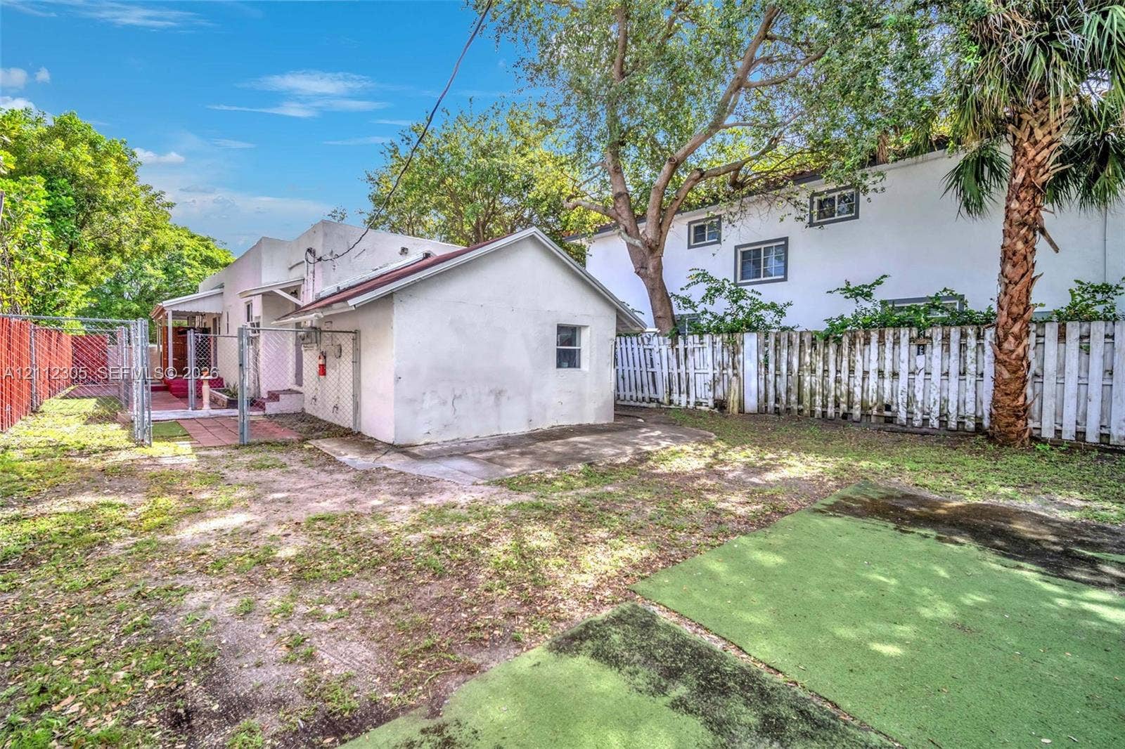 1008 N 18th Court, Hollywood, FL 33020 Exterior space featuring a detached building, paved brick patio area, chain-link and wood perimeter fencing, and mature trees