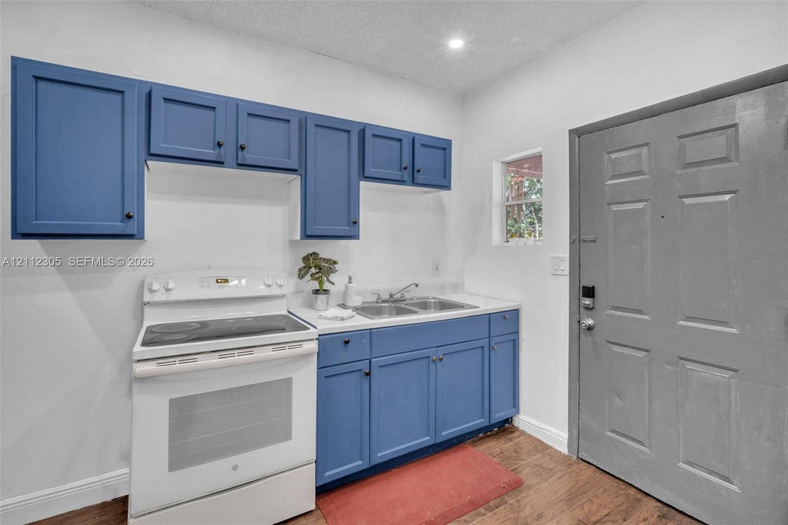 1008 N 18th Court, Hollywood, FL 33020 Blue cabinetry with shaker-style doors, white electric range, double-basin stainless steel sink, solid-surface countertop, and wood-finish flooring