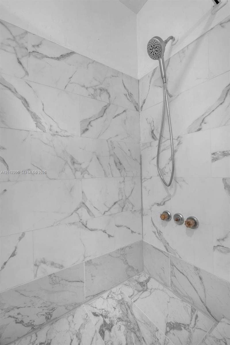 1008 N 18th Court, Hollywood, FL 33020 Shower enclosure featuring large-format veined tile surround, metallic handheld shower fixture, and circular multi-handle valve controls