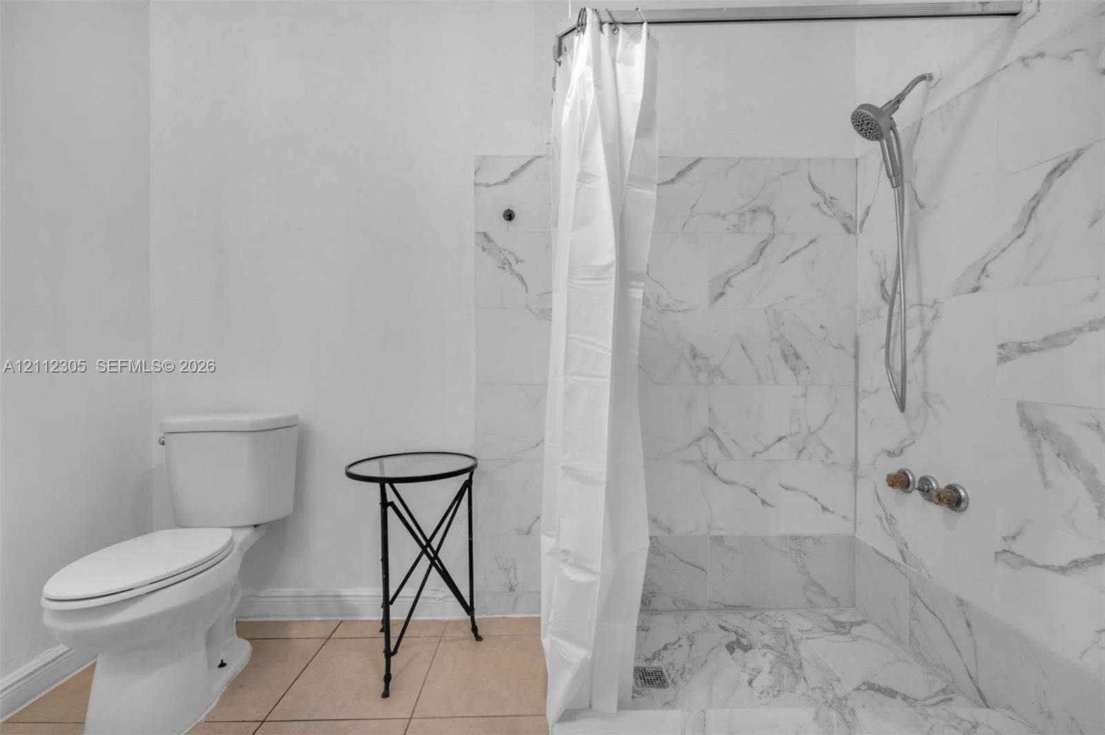 1008 N 18th Court, Hollywood, FL 33020 Walk-in shower enclosure featuring large-format wall-to-floor veined tile, handheld shower fixture, and ceramic toilet