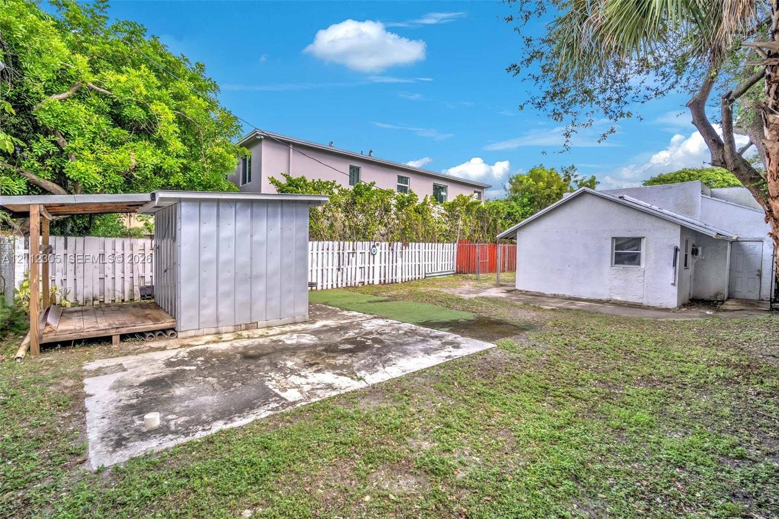 1008 N 18th Court, Hollywood, FL 33020 Fenced backyard featuring an auxiliary structure with a covered porch, an open-air concrete pad, and mature trees