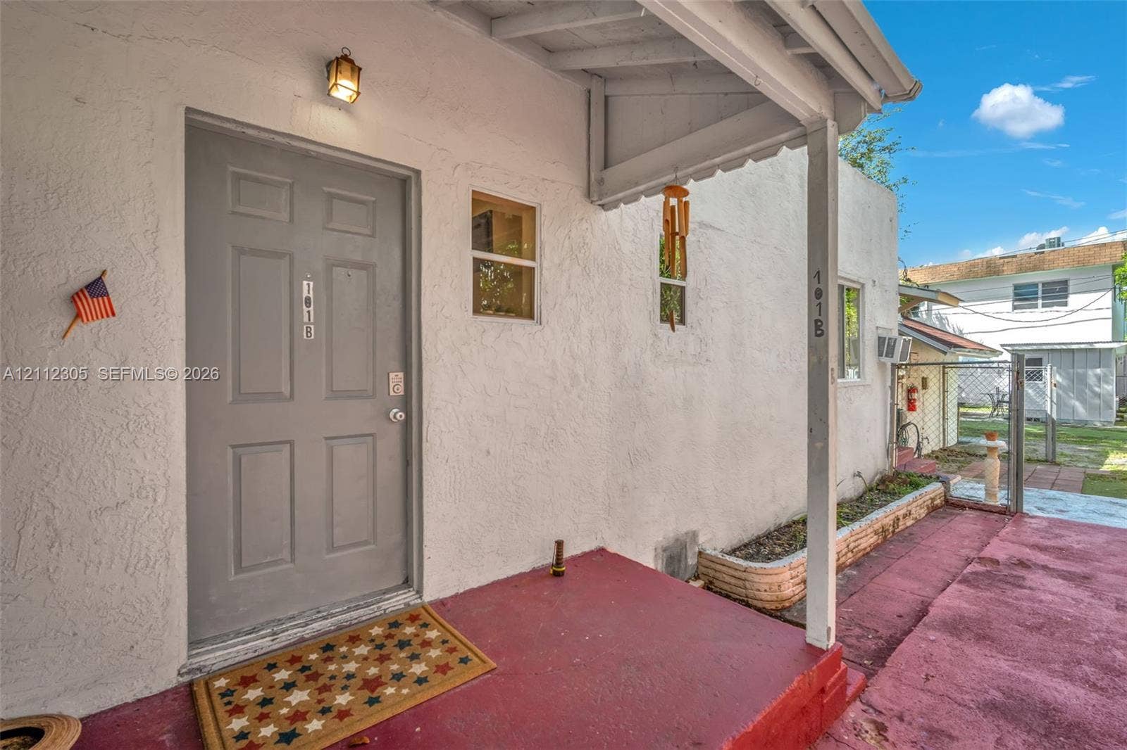 1008 N 18th Court, Hollywood, FL 33020 Covered entryway featuring a textured stucco exterior, a solid six-panel door, an exterior wall-mounted light fixture, and a masonry planter box