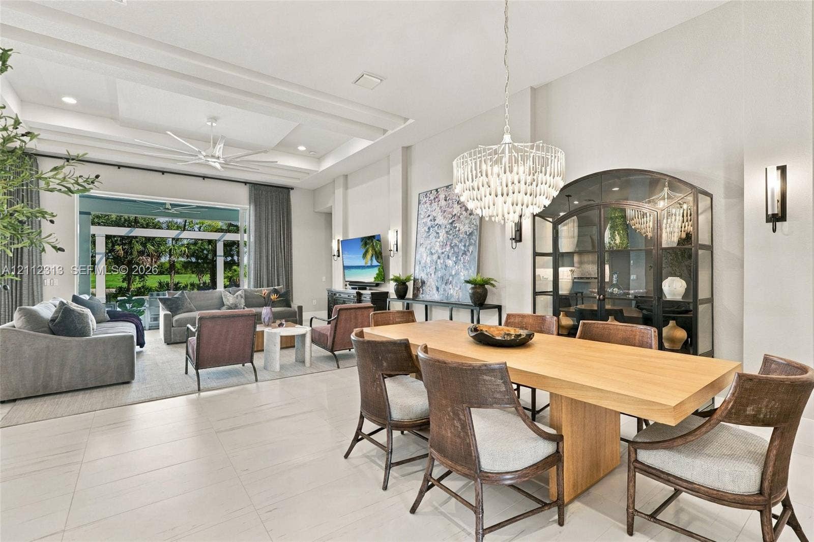 Open-concept living space featuring high tray ceilings, recessed lighting, expansive tile flooring, and a crystal chandelier