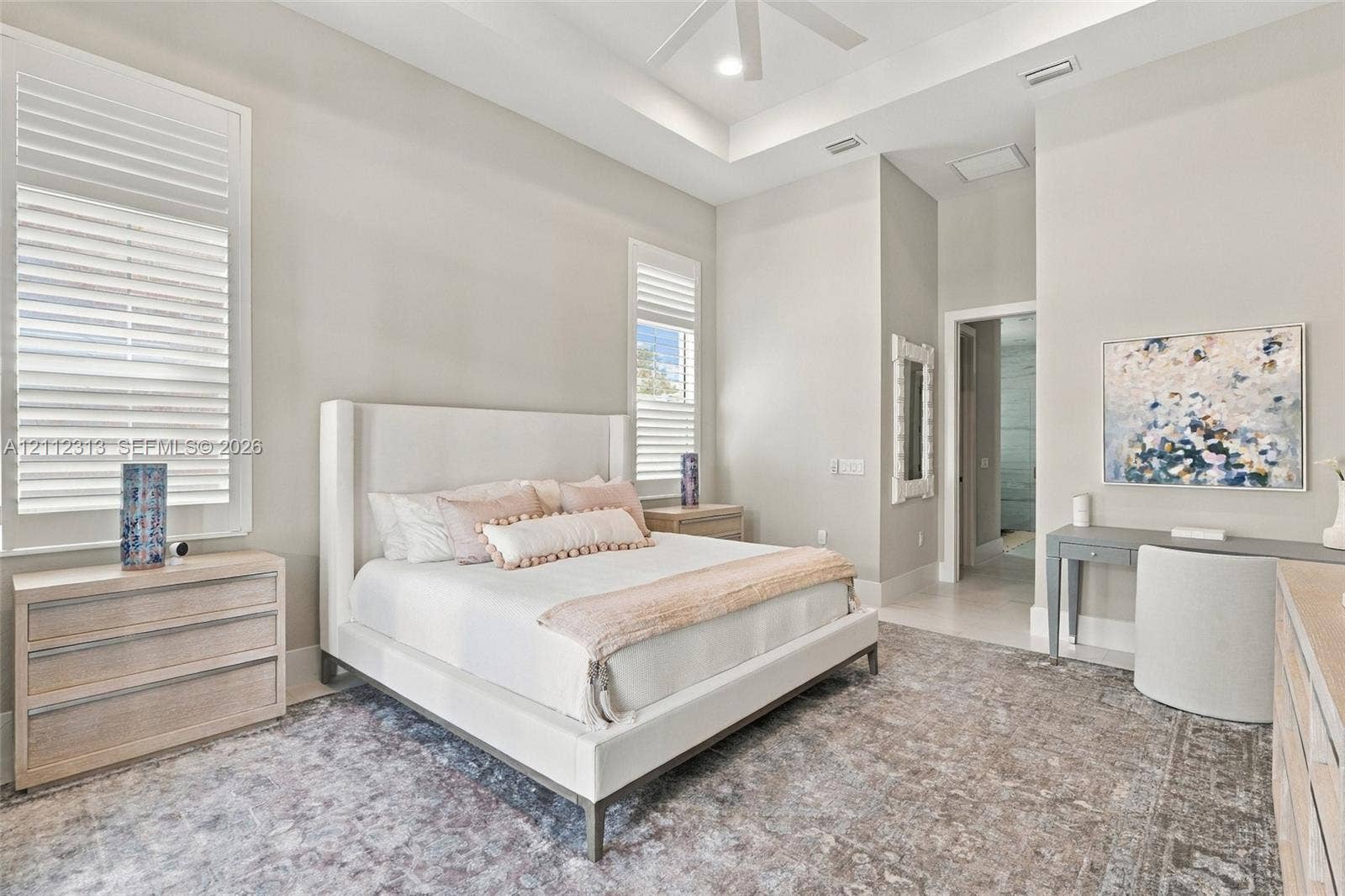High ceilings with a recessed tray detail, large windows with white shutter blinds, and a built-in ceiling fan