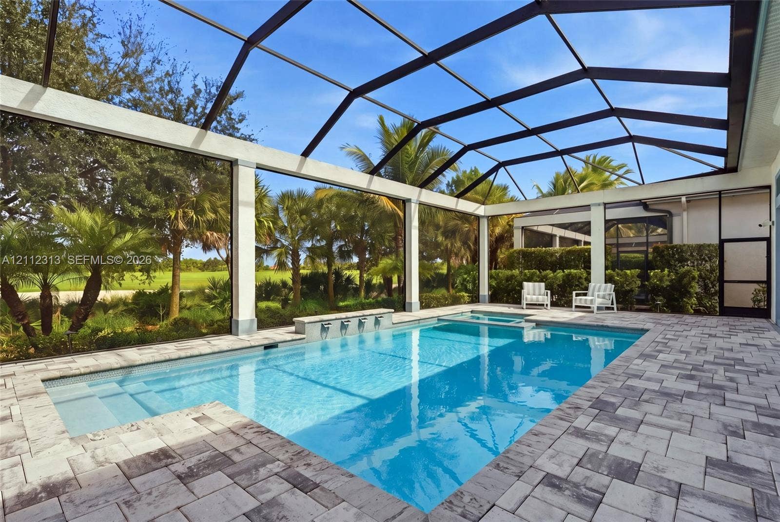 Screened pool enclosure featuring a stone-paver deck, built-in spa, and a wall fountain with multiple spillway spouts
