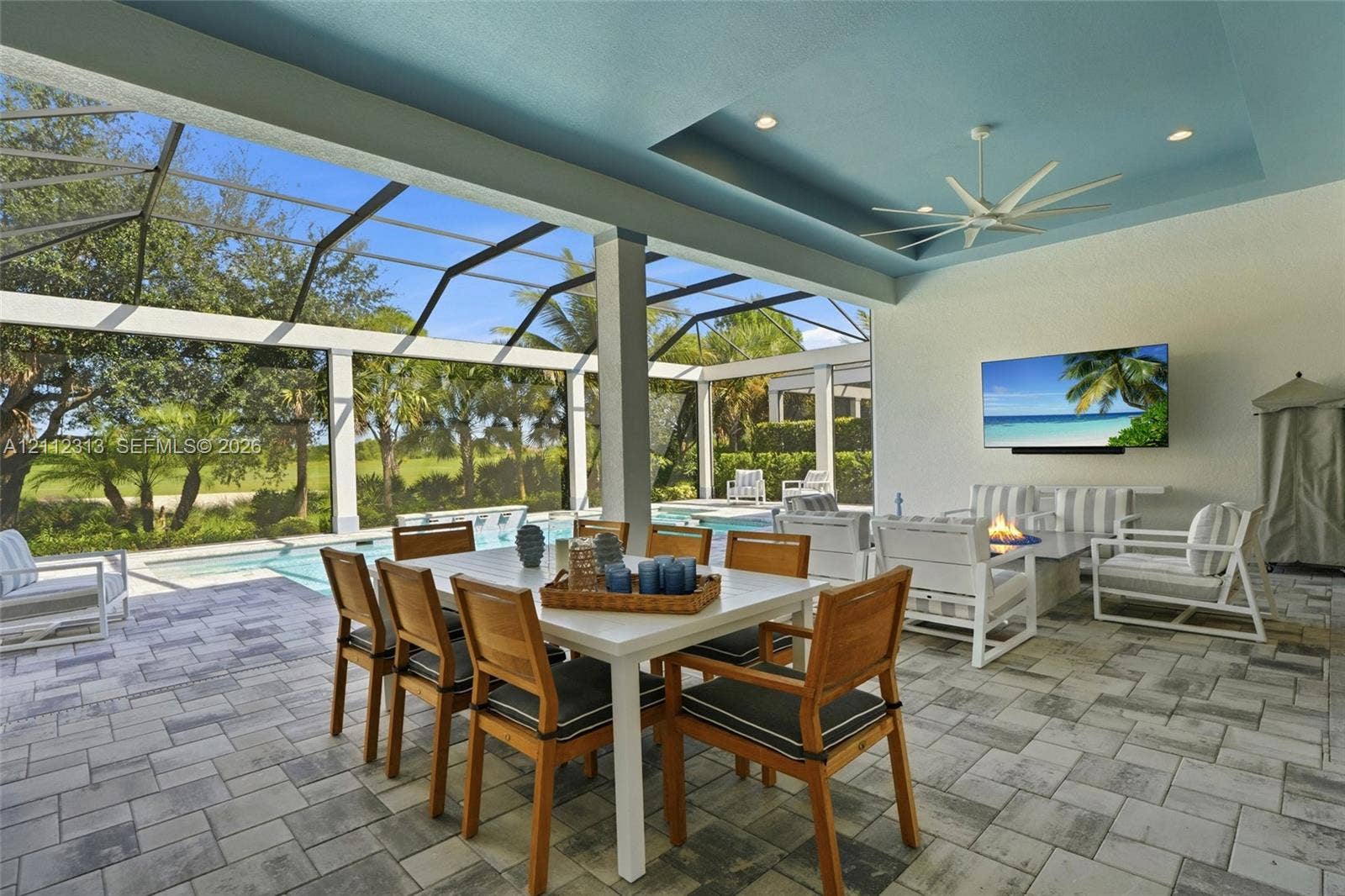 Covered lanai featuring a tray ceiling with recessed lighting, integrated ceiling fan, paver flooring, and a screen enclosure overlooking a swimming pool
