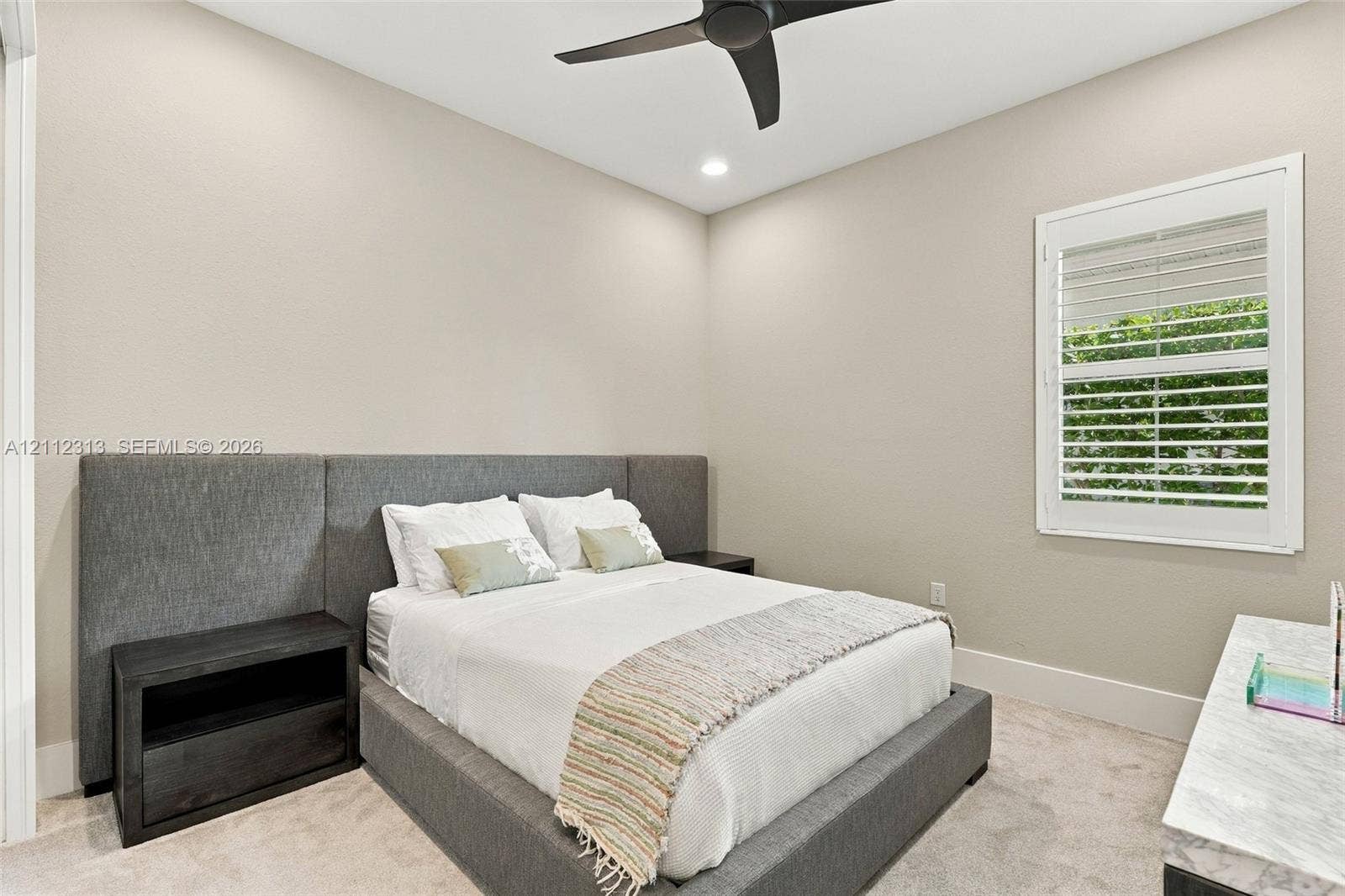 Neutral-toned room featuring a matte black ceiling fan, recessed lighting, and a single window with white plantation shutters