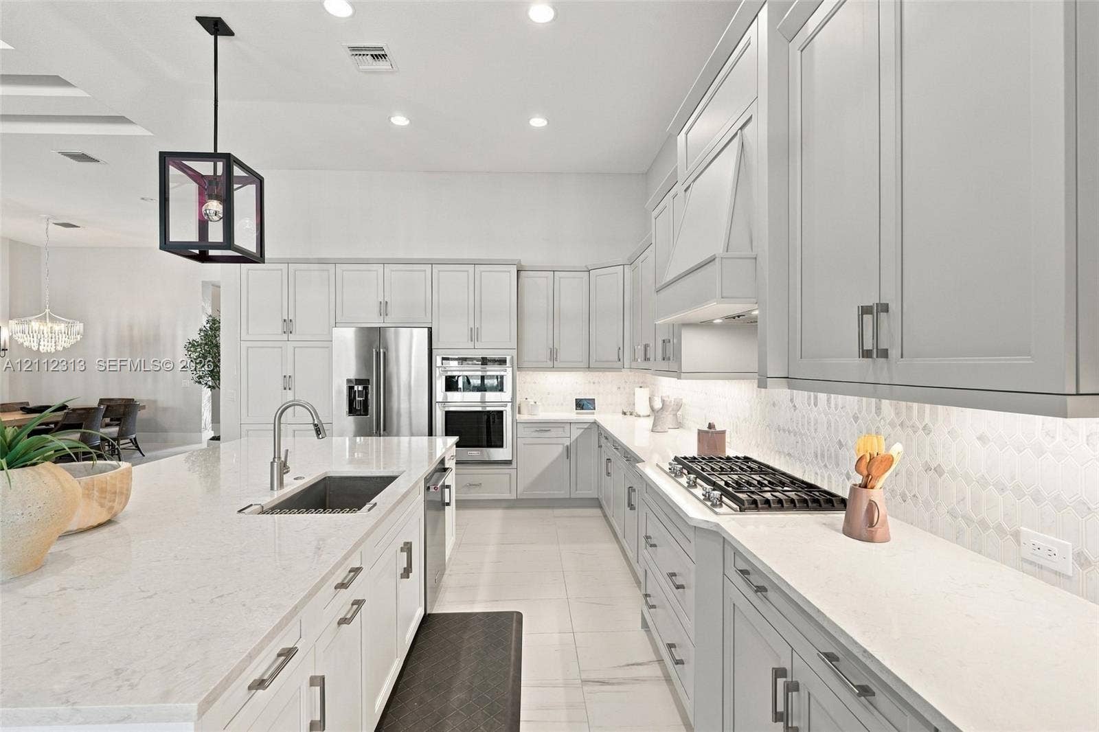 Kitchen featuring light-toned cabinetry, a spacious island with a built-in sink, stone-finish countertops, stainless steel appliances, and a geometric pendant light fixture