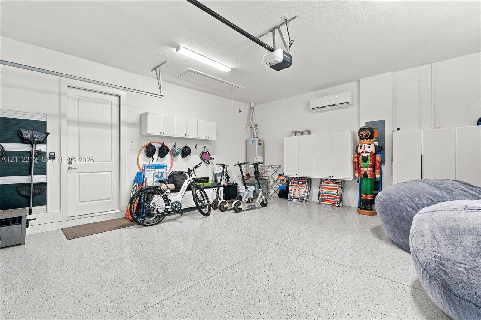 Garage featuring epoxy-coated flooring, wall-mounted white storage cabinetry, an installed climate control unit, and an automated garage door opener system