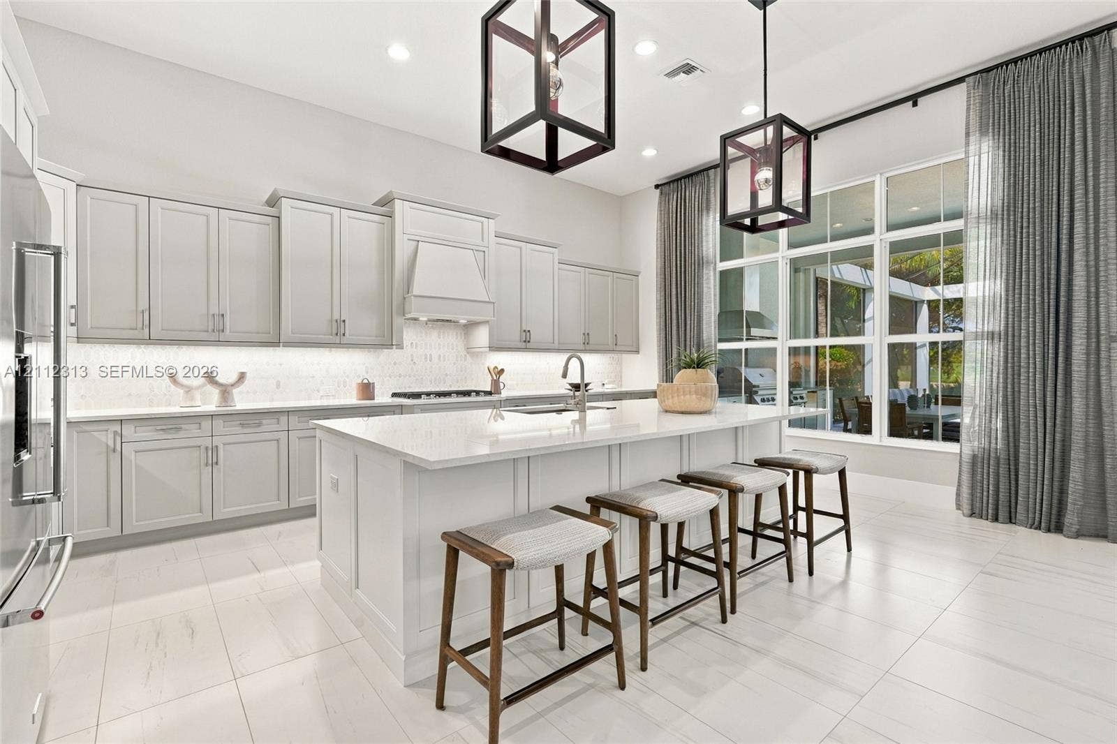 Kitchen featuring light-toned cabinetry, a large central island with a solid surface countertop, tile flooring, recessed lighting, and geometric pendant fixtures