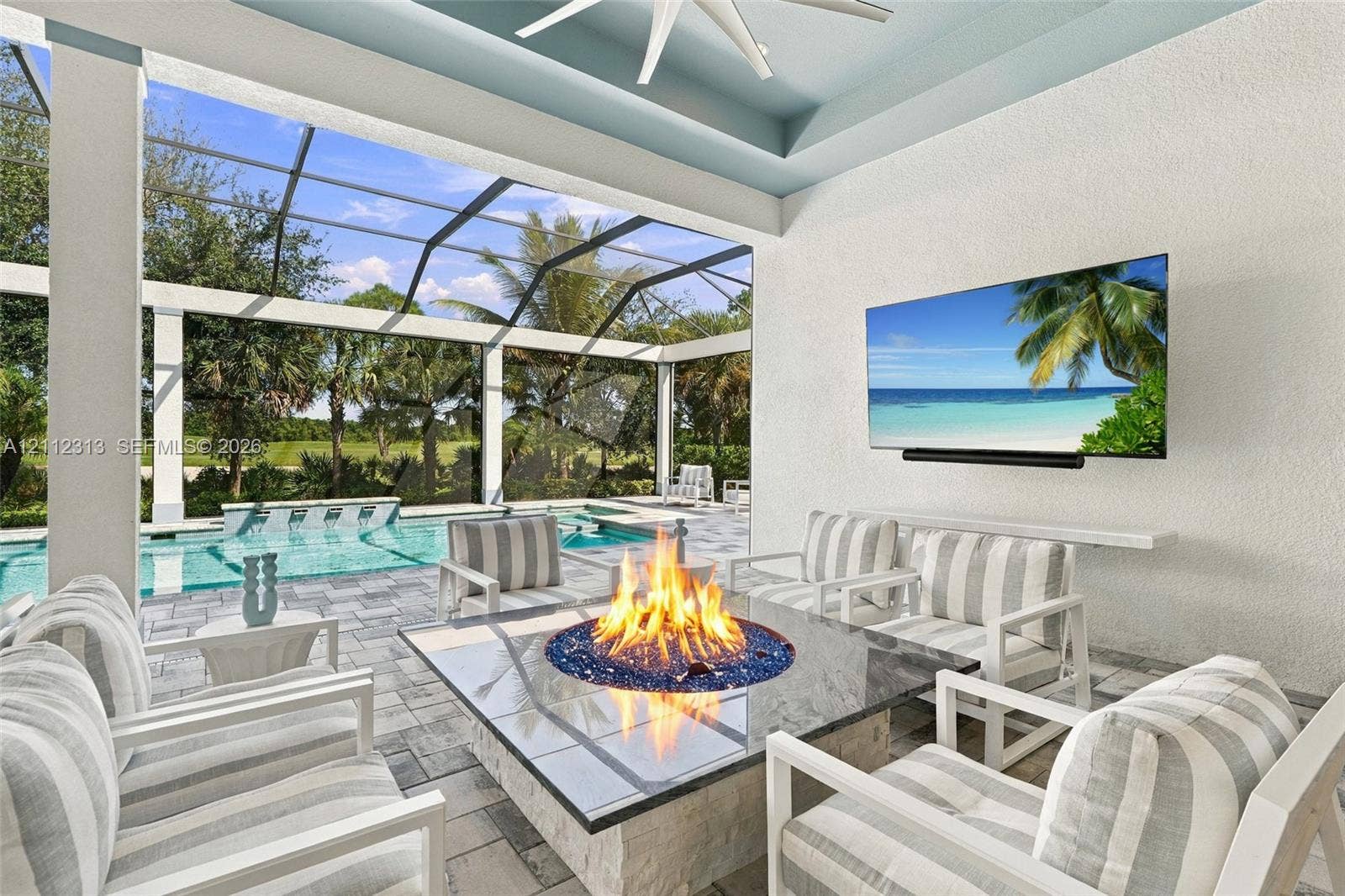 Covered lanai featuring a stone-topped built-in fire pit, screened enclosure, custom ceiling fan, and built-in wall-mounted television, accented by paver flooring and an integrated swimming pool