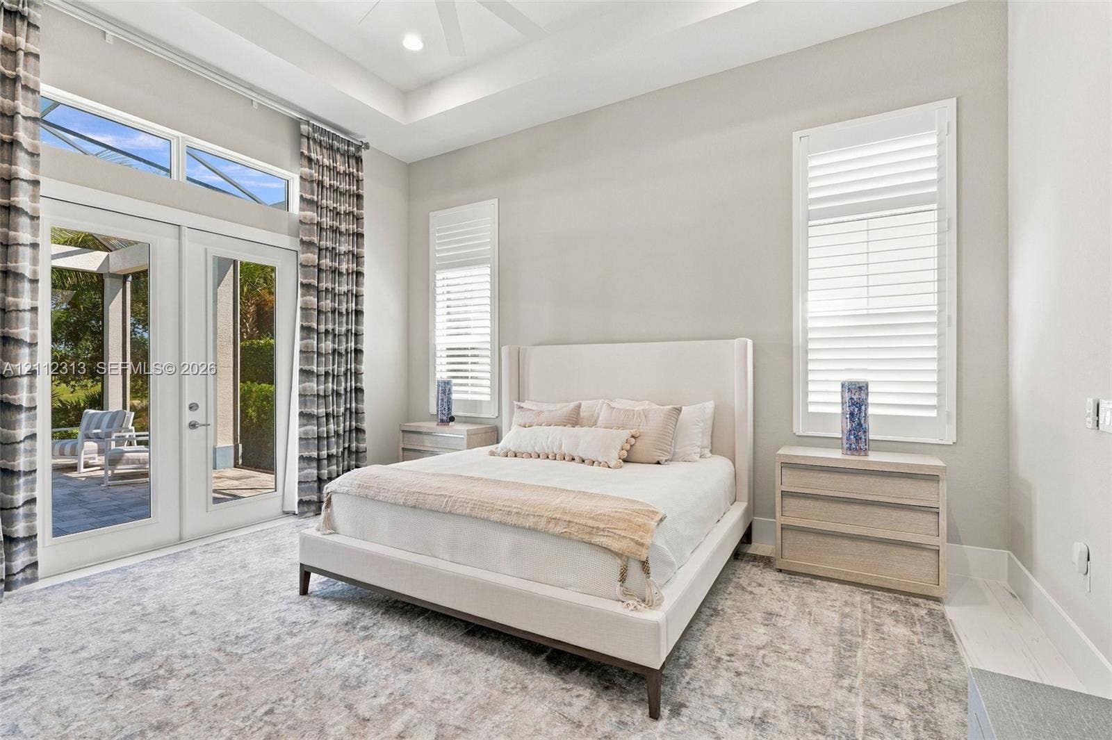 Tray ceiling with recessed lighting, floor-to-ceiling glass French doors, transom windows, and white plantation shutters