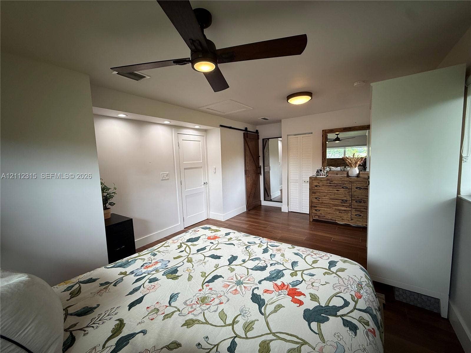 Wood-finish flooring, dark-finish ceiling fan with integrated lighting, recessed ceiling lighting, louvered-style closet doors, and wood-finish sliding barn-style door