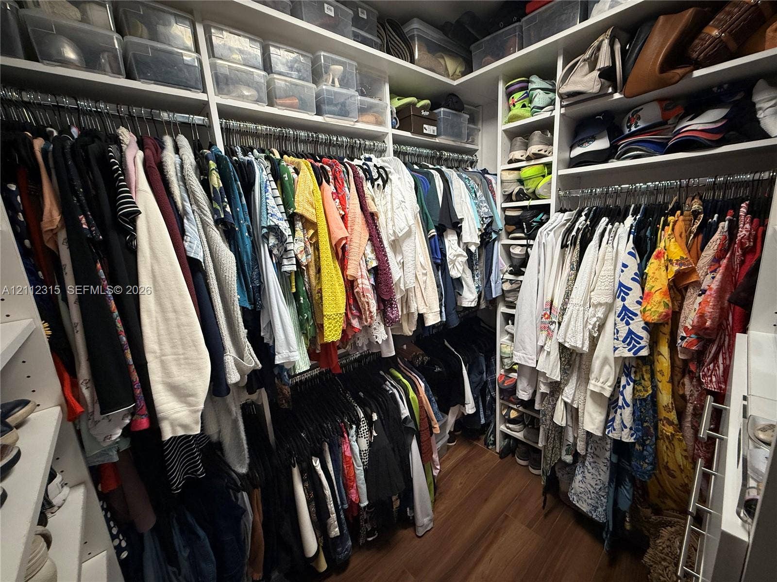 Custom walk-in closet featuring white built-in shelving, multiple tiers of hanging rods, and wood-finish flooring