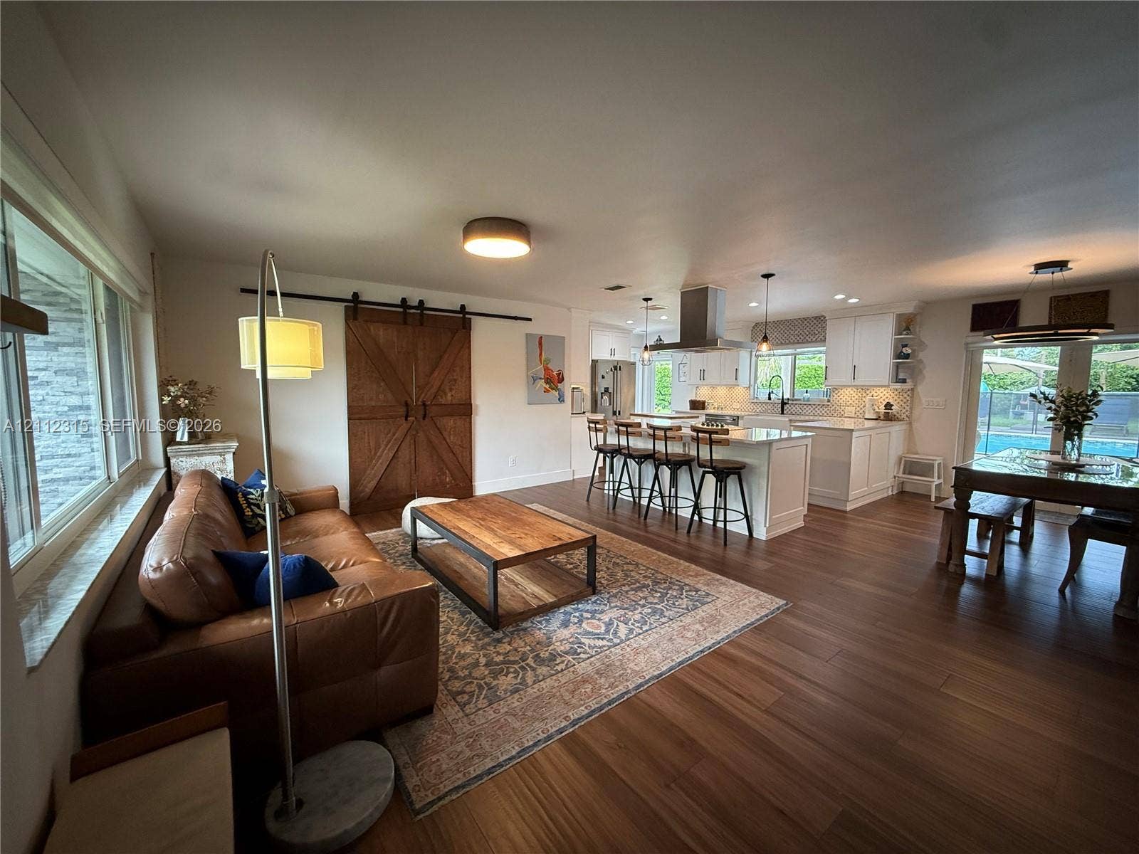 Kitchen featuring a central island with a stone countertop, white cabinetry, stainless steel range hood, and wood-finish flooring, complemented by sliding wood barn doors