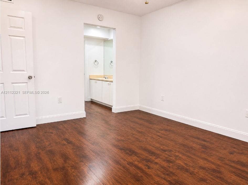 Room with wood-finish flooring, white walls, and a six-panel interior door