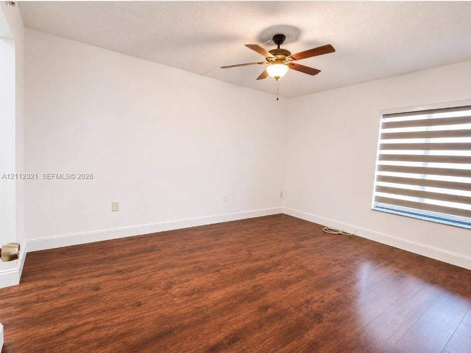 Room featuring wood-finish flooring, a ceiling fan with integrated lighting, and a window with horizontal roller shades