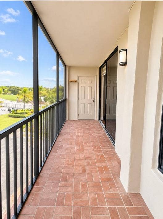 Screened-in balcony featuring terra-cotta tile flooring, black metal railings, a wall-mounted exterior light fixture, and a solid-core entry door