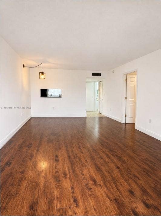 Interior space featuring dark wood-finish flooring, a wall-mounted industrial-style pendant light, and a pass-through opening