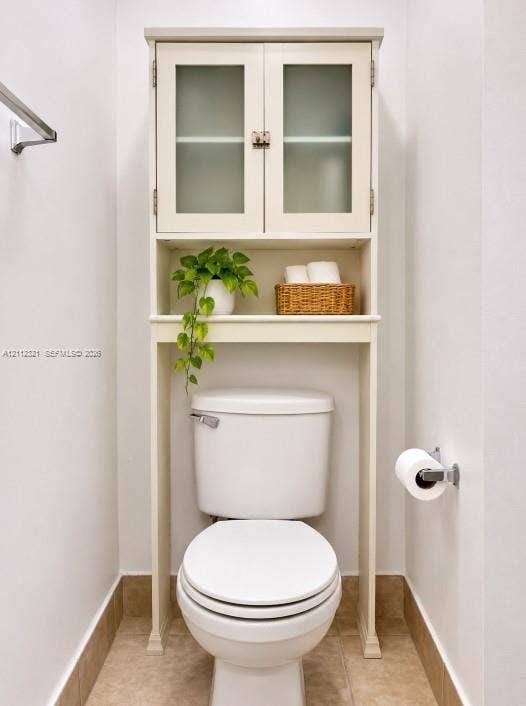 Built-in cabinetry featuring glass-panel doors and open shelving, paired with a ceramic toilet, stainless steel towel bar, and metallic toilet paper holder