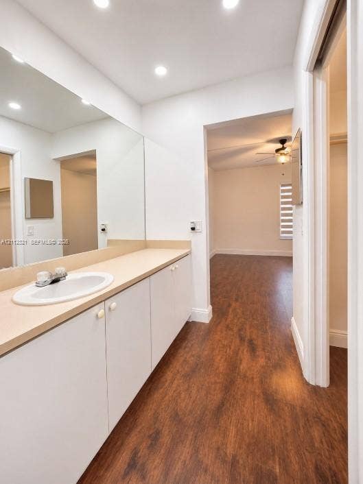 Bathroom vanity featuring white cabinetry, a solid surface countertop, an undermount oval sink, and a full-width wall mirror, complemented by wood-finish flooring