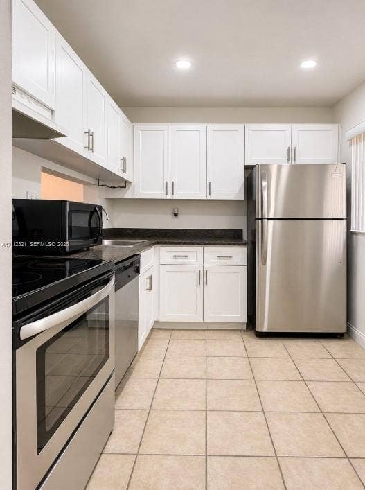 Kitchen featuring white Shaker-style cabinetry, dark stone-finish countertops, stainless steel appliances, and ceramic tile flooring