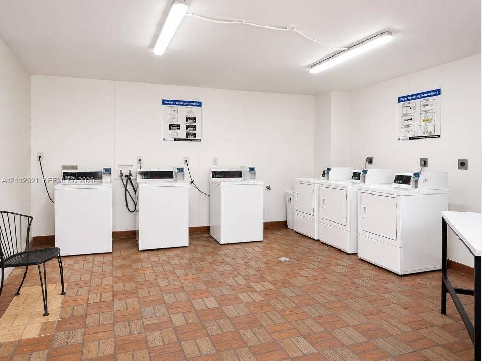 Laundry area featuring multiple coin-operated washing machines and dryers with ceramic tile flooring and linear fluorescent lighting