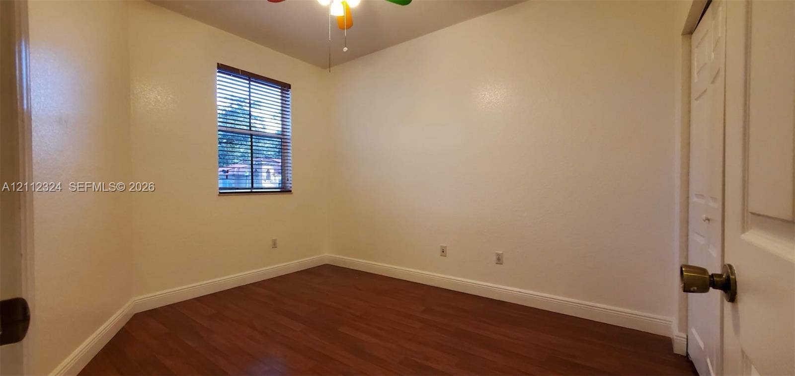 Room featuring wood-finish flooring, a single-panel interior door, horizontal window blinds, and a central ceiling light fixture