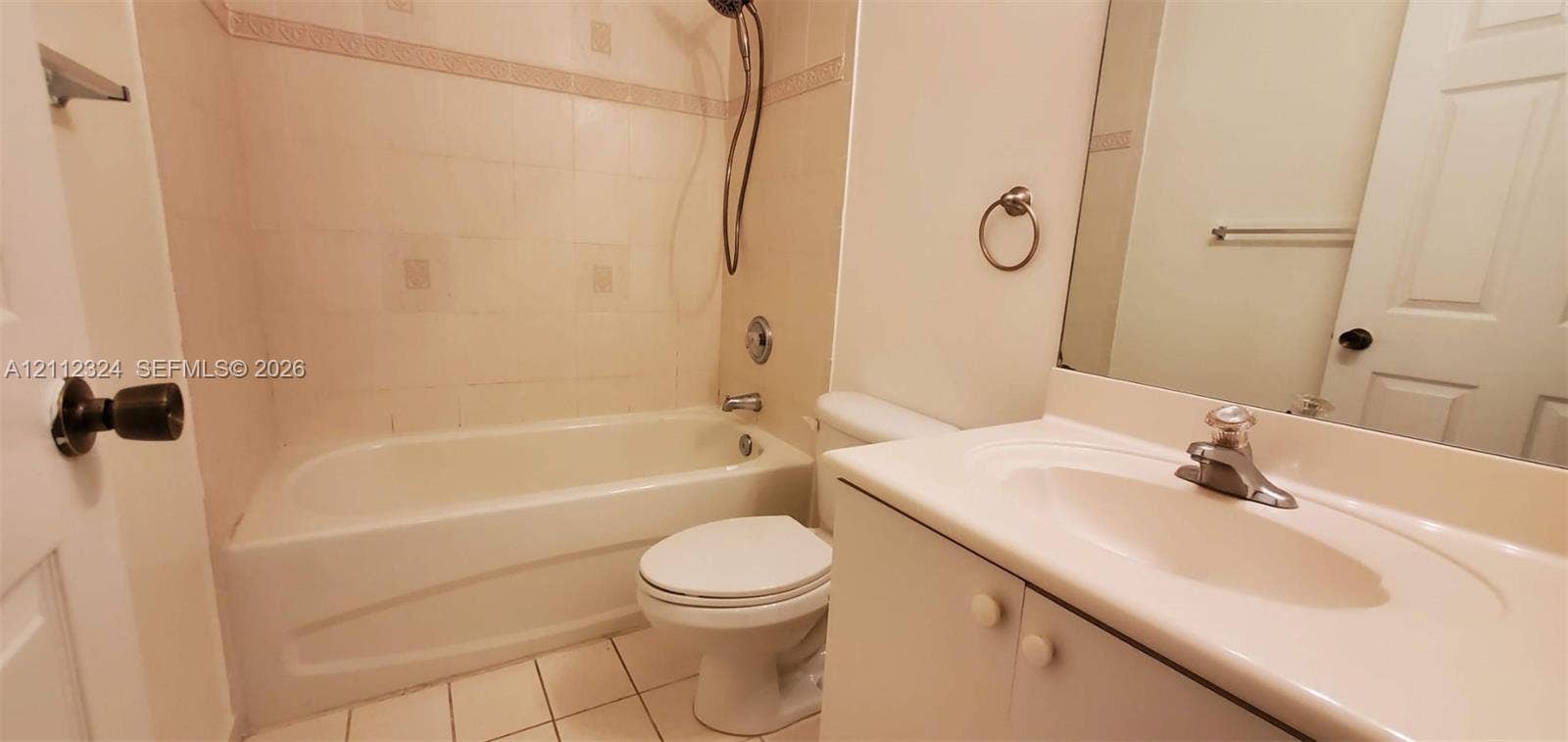 Bathroom featuring a white molded vanity with an integrated basin, wall-mounted mirror, ceramic tile flooring, and a shower-tub combination with tiled surround
