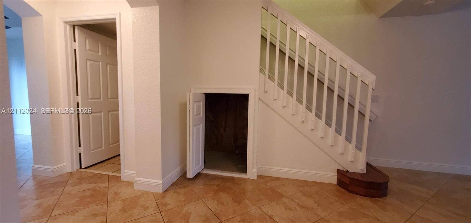 Interior area featuring ceramic tile flooring, a staircase with a white wood-finish balustrade, and a built-in under-stair storage compartment with a solid panel door