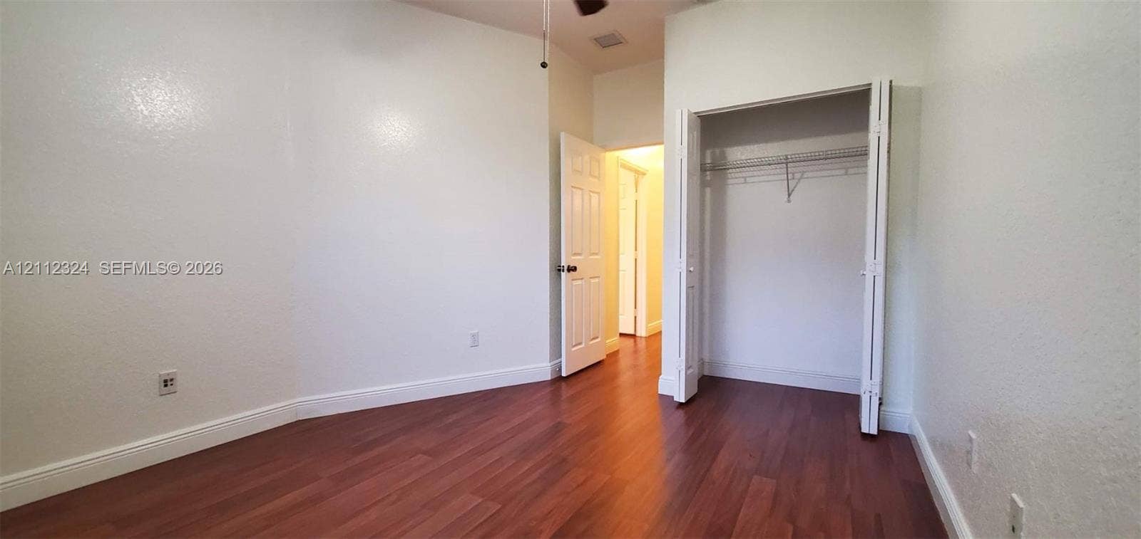 Room featuring wood-finish flooring, textured walls, a ceiling fan, and a built-in closet with wire shelving