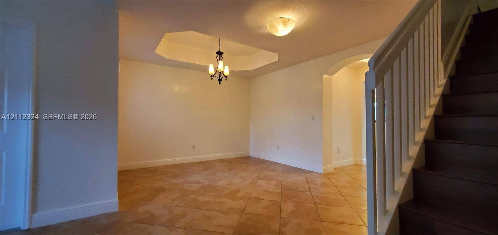 Tiled flooring, tray ceiling, decorative multi-light chandelier, arched doorway, and staircase with wooden treads and white balusters