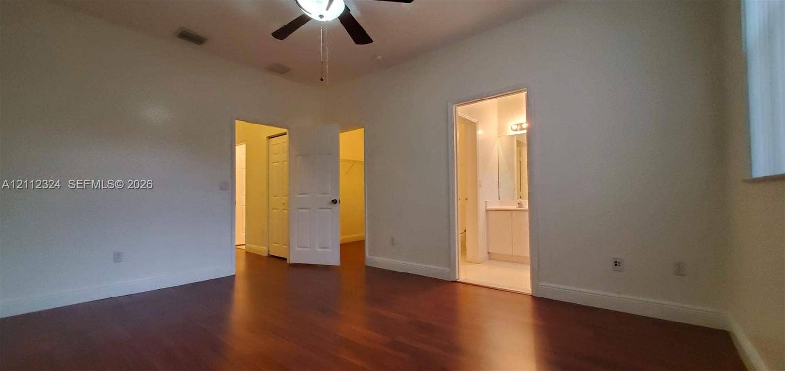 Interior space featuring wood-finish flooring, high ceilings, ceiling fan with integrated lighting, and white six-panel doors