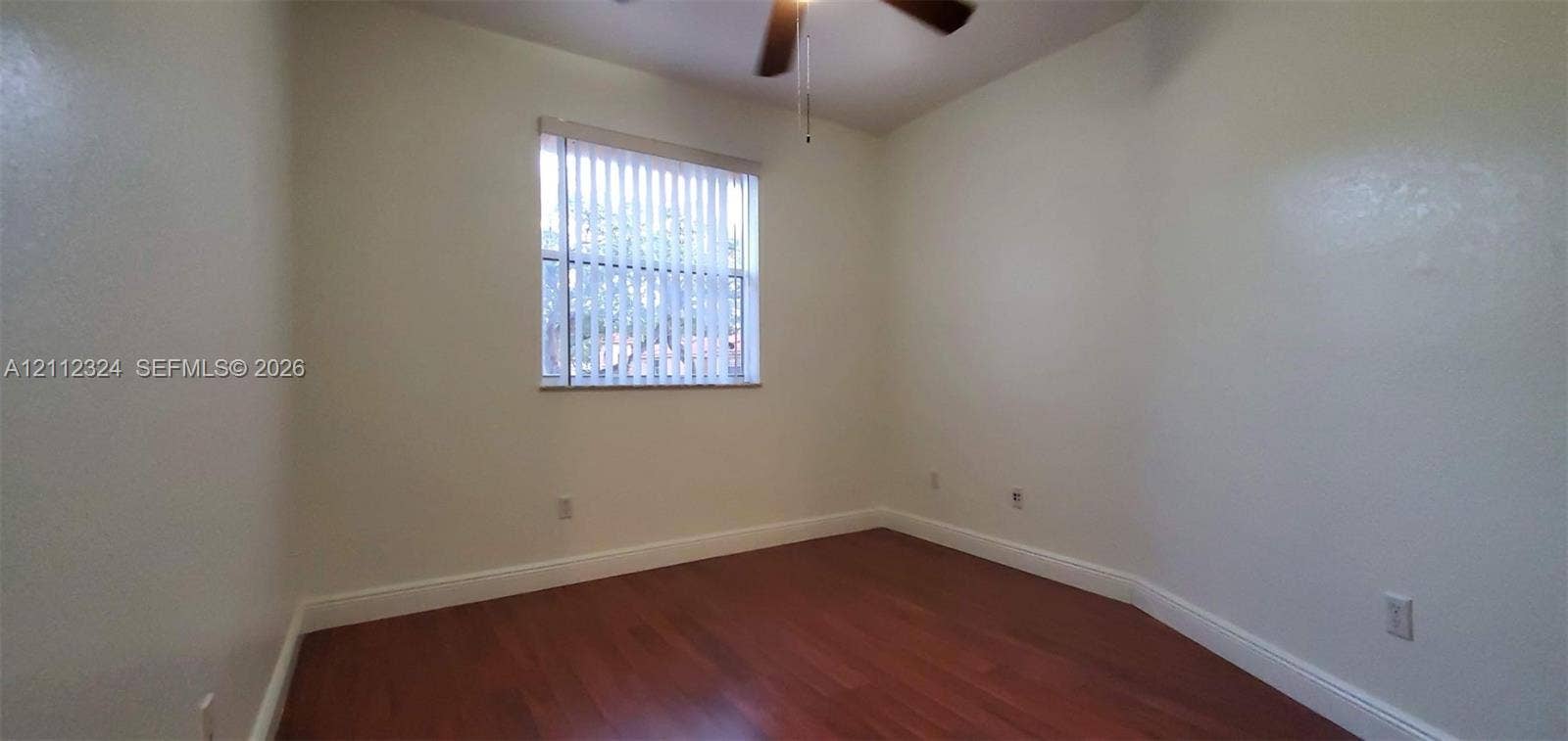Neutral-toned room featuring wood-finish flooring, a single-pane window with vertical blinds, and a ceiling fan
