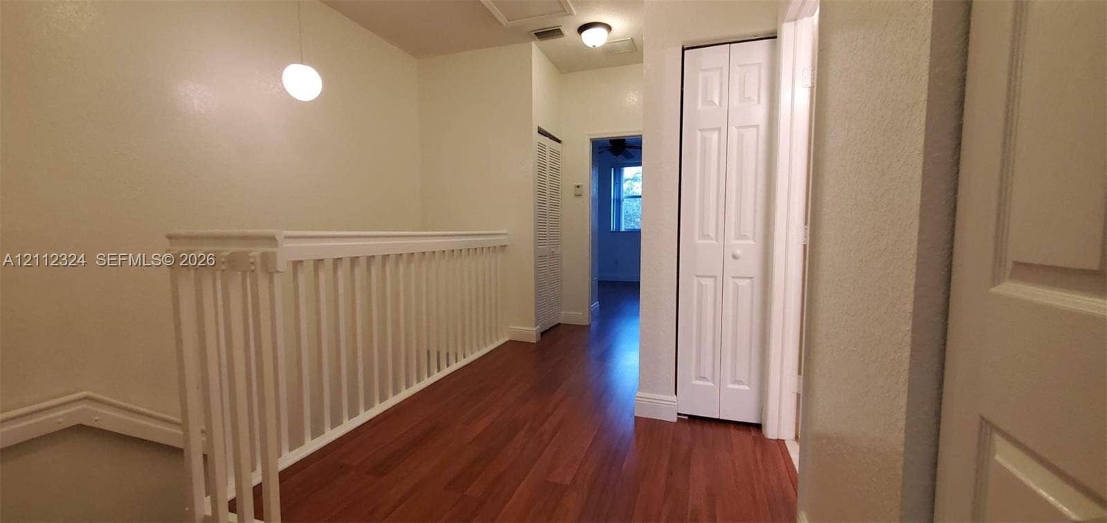 Hallway featuring wood-finish flooring, white spindle railing, flush-mount lighting, and dual bifold closet doors