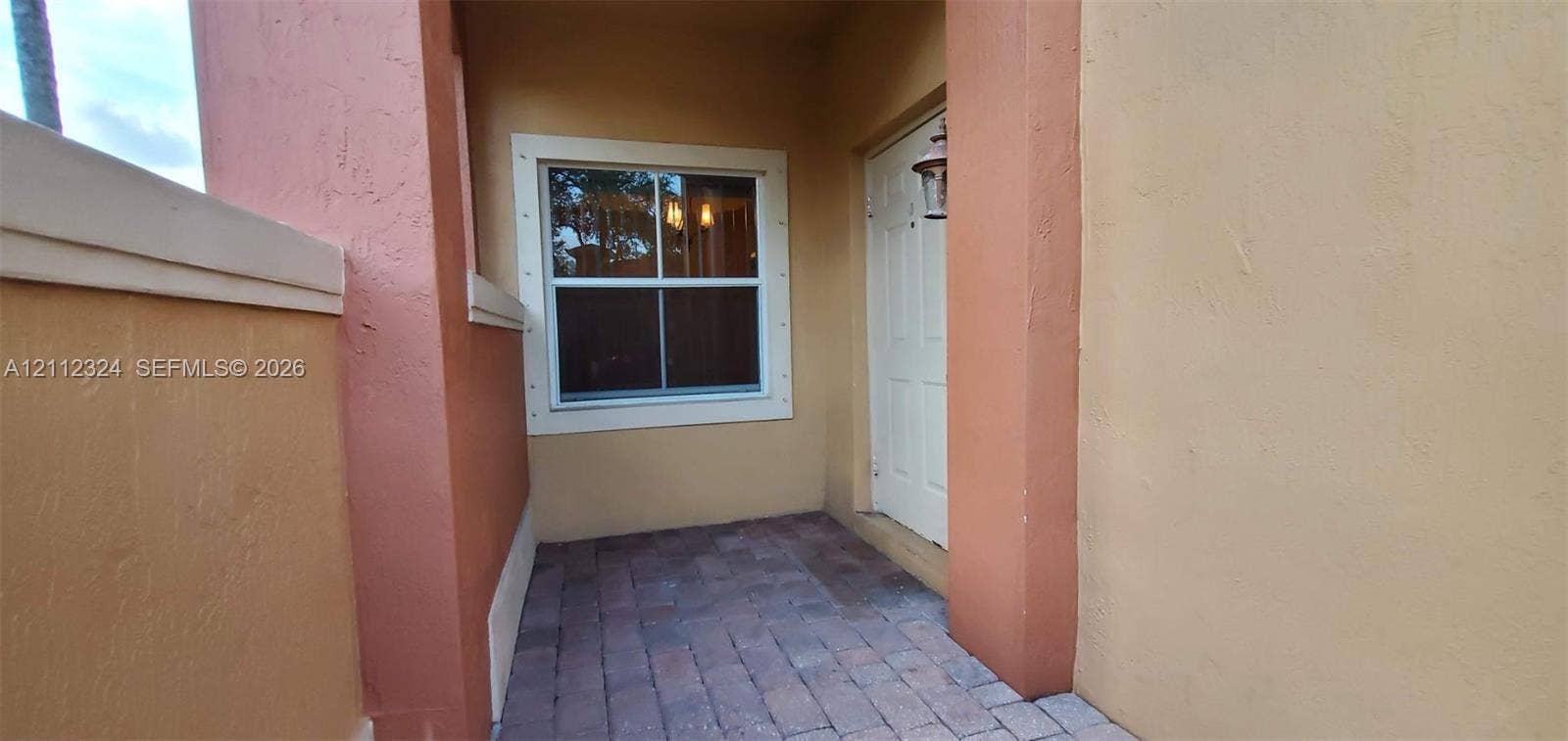 Covered entry featuring paver flooring, stucco exterior walls, and a single-pane window with trim