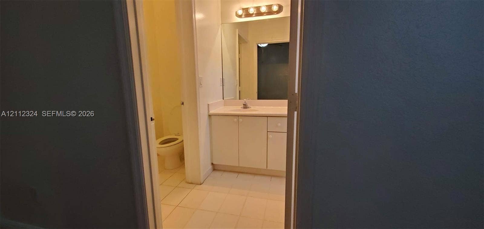 Bathroom featuring a white vanity cabinet, a solid surface countertop with an integrated sink, a large wall-mounted mirror, and tile flooring